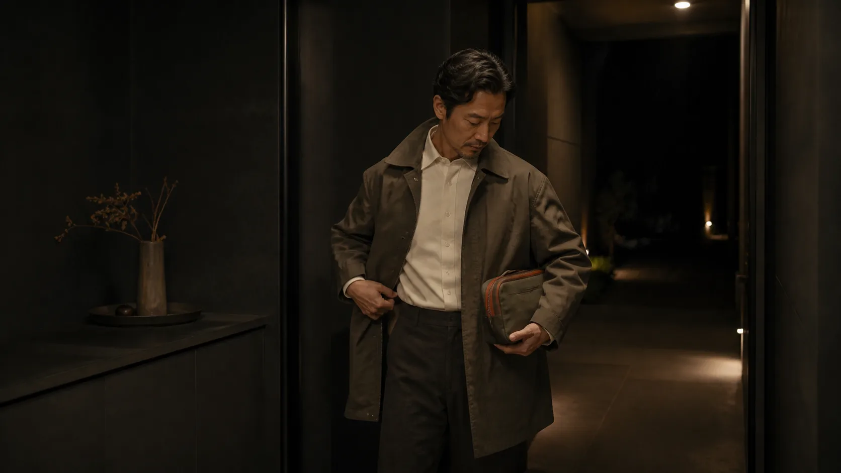현관에서 가벼운 겉옷과 작은 가방을 준비하며 퇴근 이동 조건을 점검하는 남성