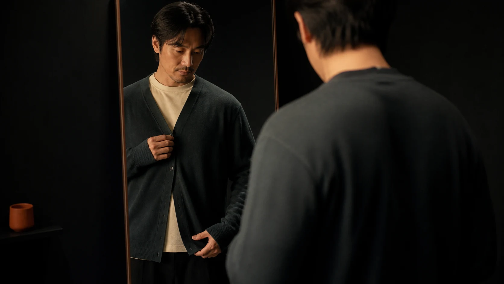 기준 이너 위 카디건의 단추 여밈과 소매 끝을 거울 앞에서 확인하는 남성