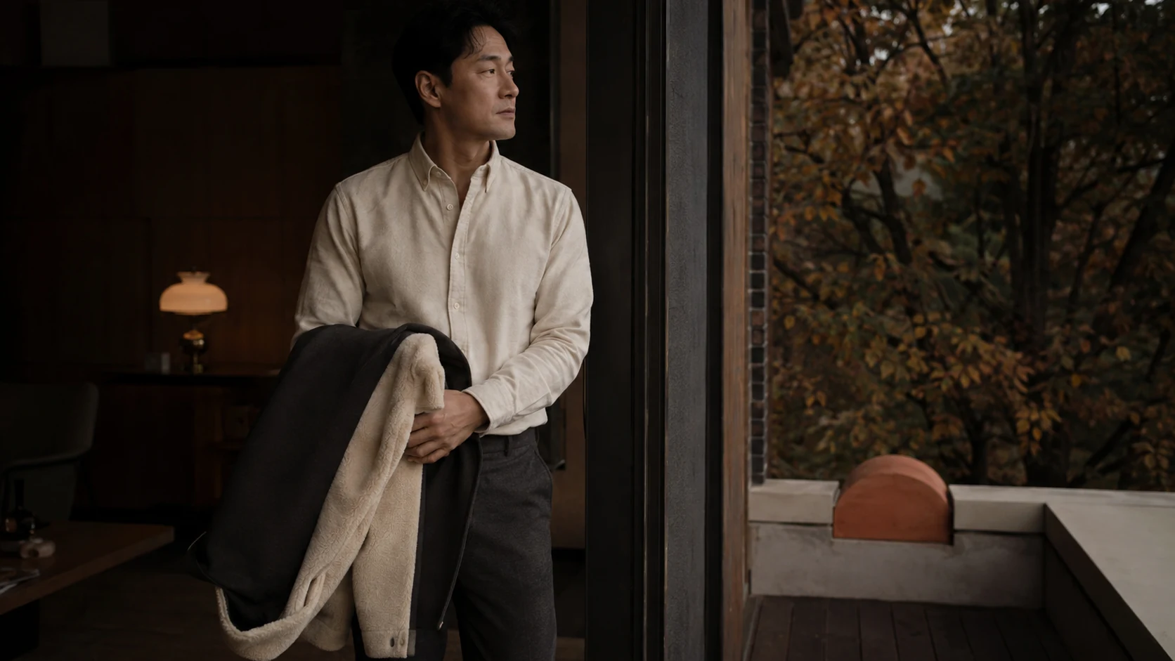 테라스와 실내 사이에서 겉옷과 외부 노출 구간을 살피는 남성