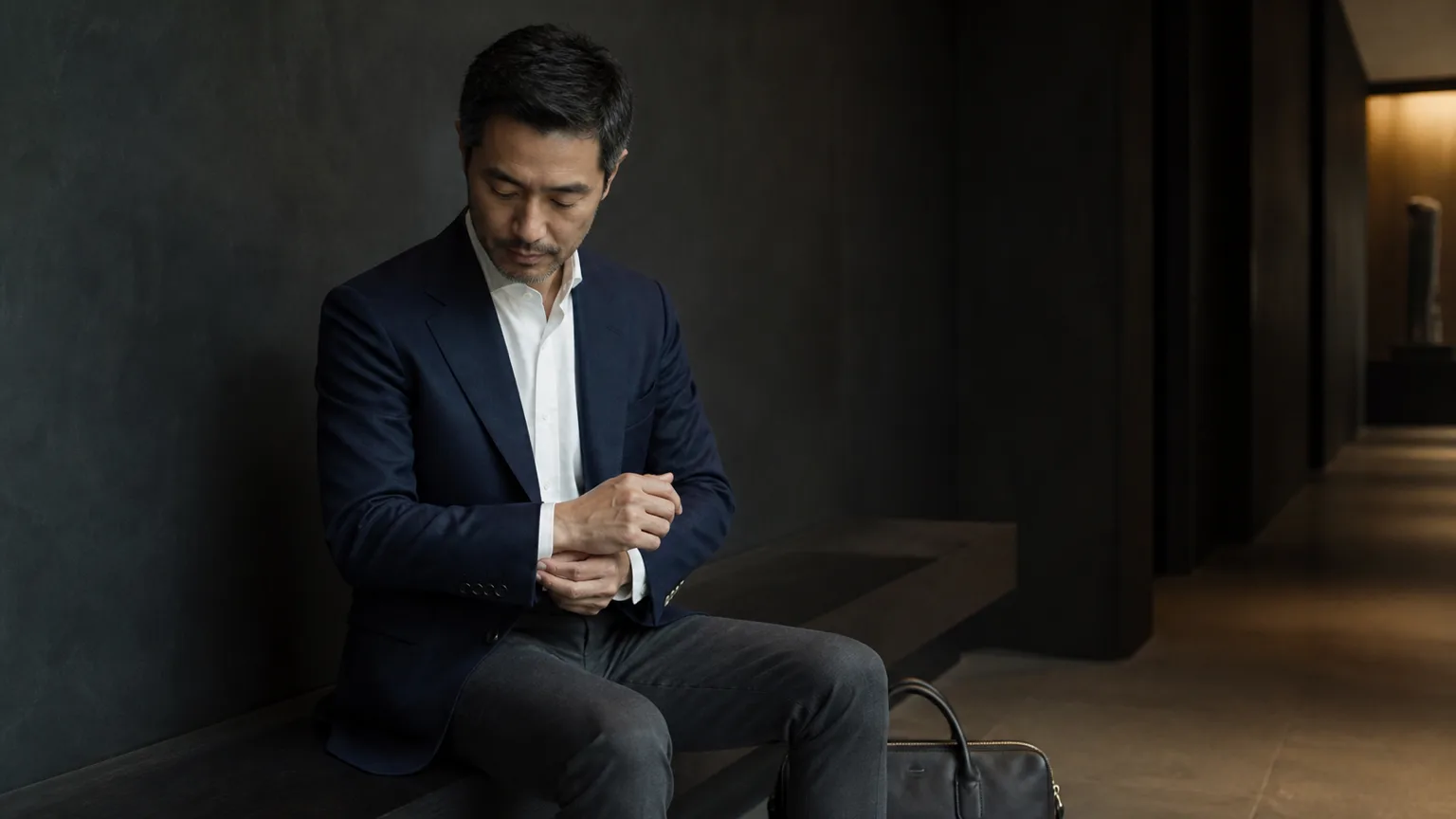 의자에 앉아 재킷 소매와 착용 상태를 점검하는 남성