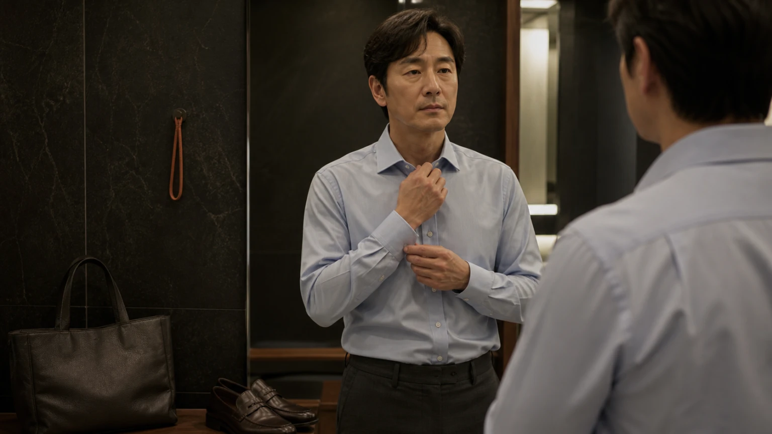 사무실 거울 앞에서 셔츠 칼라와 소매 상태를 점검하는 남성