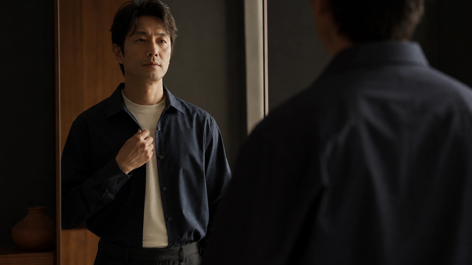거울 앞에서 열린 칼라 셔츠의 여밈과 이너 목선을 확인하는 남성