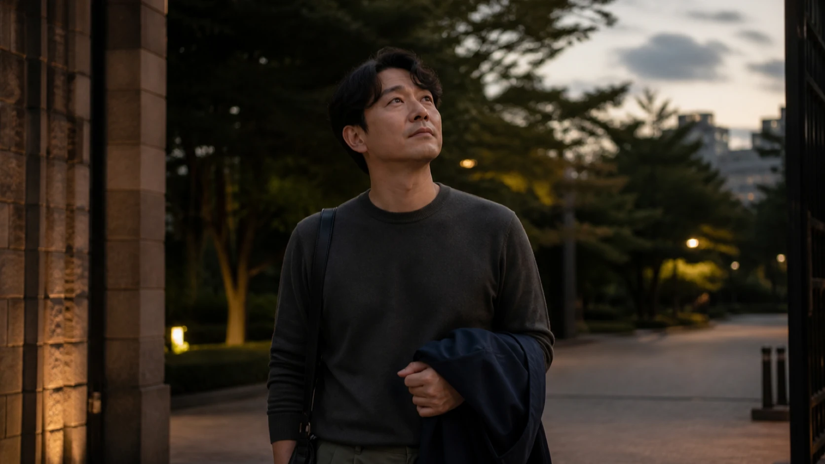 저녁 야외 공간에서 가벼운 겉옷을 들고 출발 전 날씨를 살피는 남성